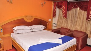 A hotel room with a wooden bed, white bedding, a blue blanket, a red armchair, and a red carpet. - Hotel Sathyam (Pudukkottai)