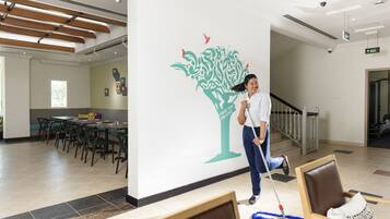 Una persona limpiando el suelo de un pasillo, con un mural decorativo en la pared, una escalera y un comedor al fondo.