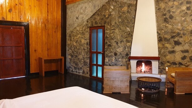 A cozy room with a stone wall, a wooden door, a fireplace, and a bed. - Auberge Plain of Jars - Phouphadeng (Phonsavan)