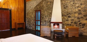 A cozy room with a stone wall, a wooden door, a fireplace, and a bed. - Auberge Plain of Jars - Phouphadeng (Phonsavan)