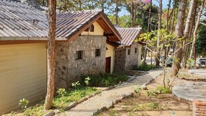 A rustic cabin with a stone exterior and a metal roof, surrounded by trees and a paved path. - Auberge Plain of Jars - Phouphadeng (Phonsavan)