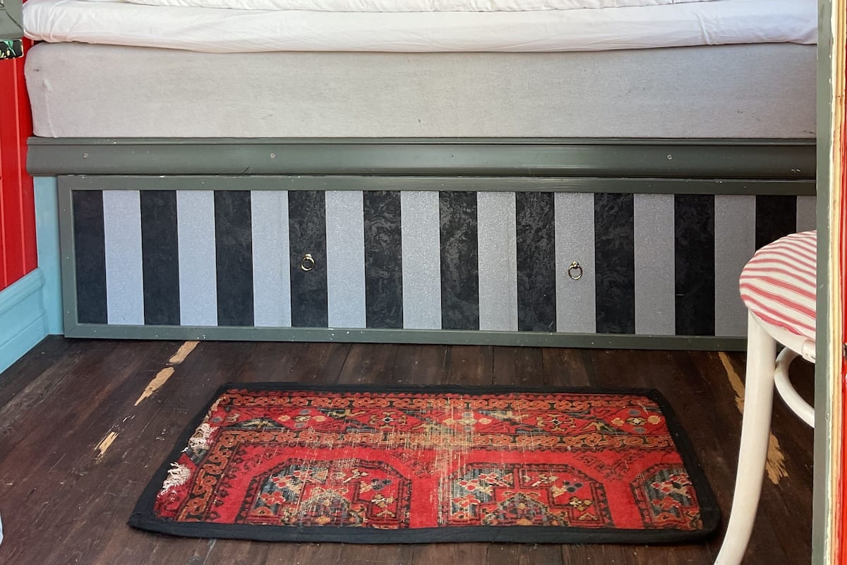 A bed with striped headboard and footboard, a red and black patterned rug, and a welcome sign on the bed.