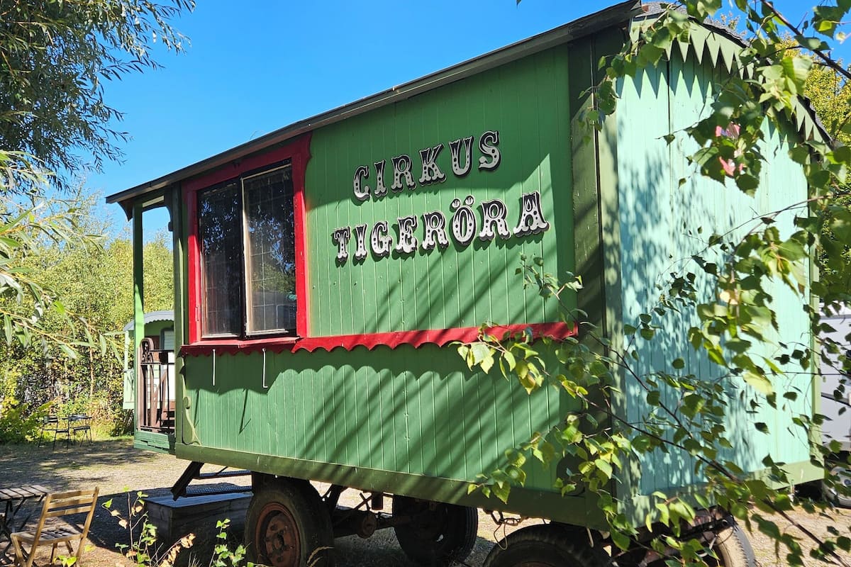 A green and red mobile circus tent with the name "CIRKUS TIGERÖRÄ" on its side, parked on a gravel path surrounded by trees.