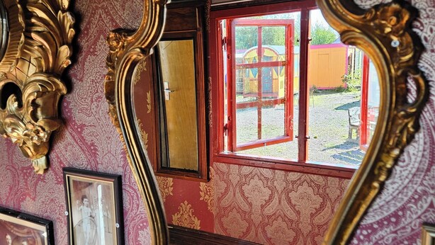 Ein Zimmer mit aufwendig verzierten, goldfarbenen Spiegeln, einem Holz-Waschtisch und ornamentalem Wandpapier.