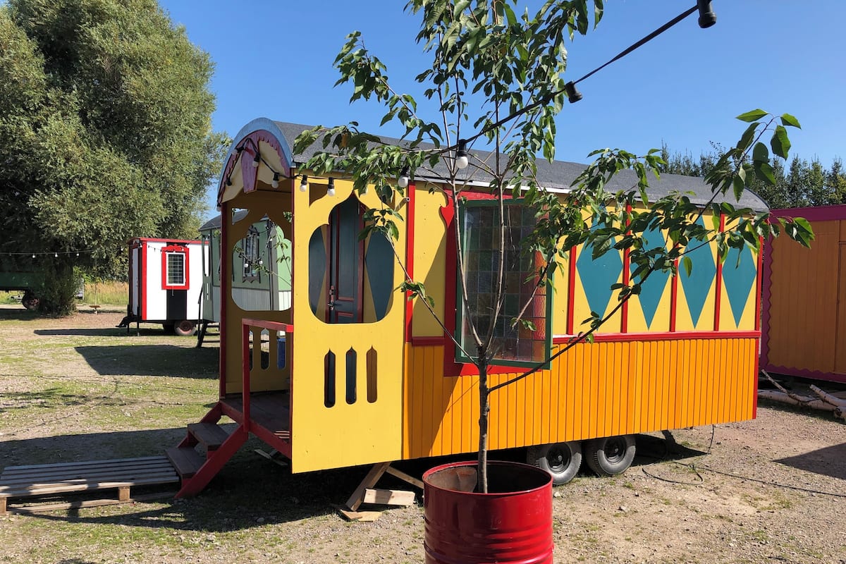 A colorful playhouse with a slide, a red barrel, and a tree in front.