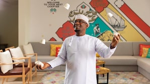 A person in traditional attire juggling cups in a living room with a colorful mural on the wall. - Atana Stay Al Ashkarah (Al Ashkharah)