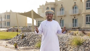 A person in traditional attire standing in front of a building with a large, open courtyard. - Atana Stay Al Ashkarah (Al Ashkharah)