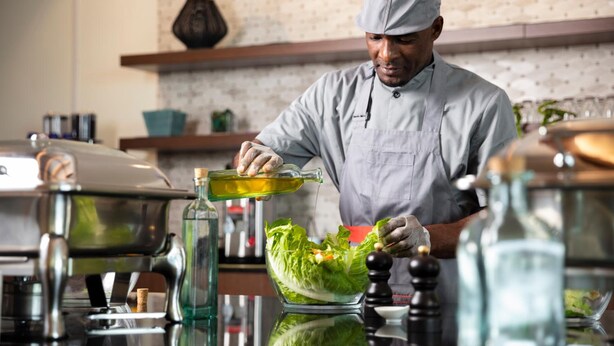 A chef preparing a salad with a bottle of dressing. - Atana Stay Al Ashkarah (Al Ashkharah)