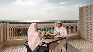 Two people dining on a balcony with a pool view. - Atana Stay Al Ashkarah (Al Ashkharah)
