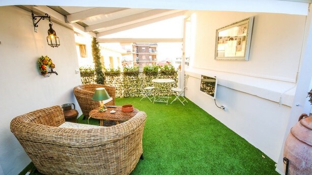 Un espacio al aire libre acogedor con mobiliario de mimbre, una mesa pequeña y césped artificial verde.