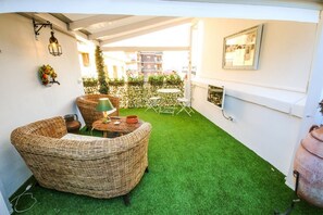 A cozy outdoor seating area with wicker furniture, a small table, and a green artificial lawn. - 96 Guest House (Reggio Calabria)