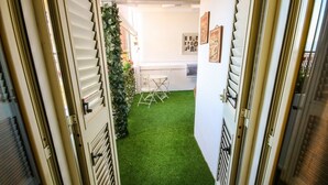Un pasillo estrecho con césped artificial verde, una silla plegable de metal y una pequeña mesa.