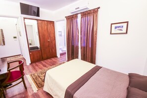 A bedroom with a bed, a chair, a desk, a television, and a bathroom visible through an open door. - 96 Guest House (Reggio Calabria)