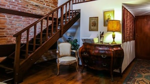 Una escalera con barandillas de madera que conduce a una zona de descanso con una silla, un aparador de madera y una lámpara.