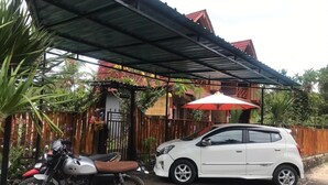 A covered parking area with a motorcycle and a white car parked under a red umbrella. - Putra Bali Villa (Penida Island)