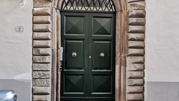A green double door with a decorative archway, a metal gate above it, and a number '2' sign on the wall. - Chalet Lucca (Lucca)