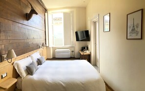 A hotel room with a wooden headboard, a bed with white linens, a flat-screen TV mounted on the wall, and a framed picture of the Eiffel Tower. - Chalet Lucca (Lucca)