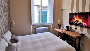A hotel room with a bed, a desk, a TV with a fireplace, a window, and a radiator. - Chalet Lucca (Lucca)