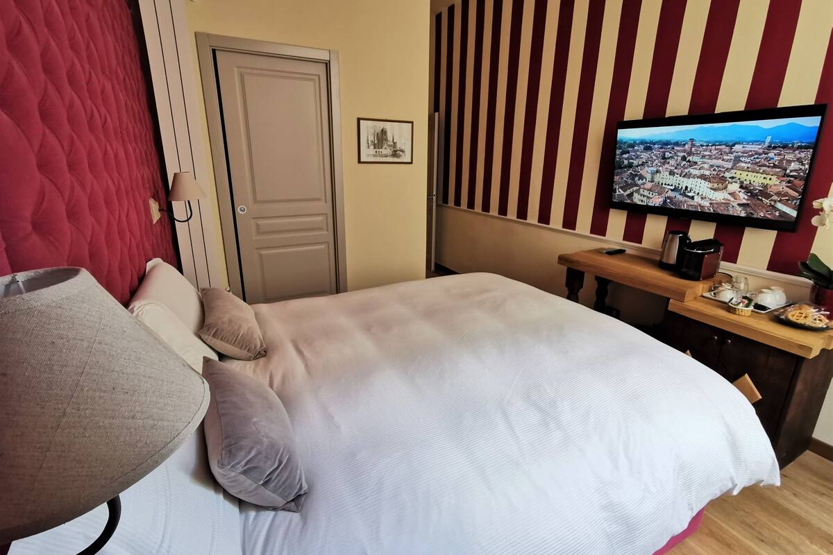 A hotel room with a bed, a TV, a wooden side table with amenities, a red curtain, and a door.