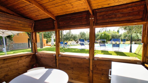 A covered outdoor seating area with a pool view, wooden walls, and a white table. - B&B Casale Ansamagi Relax & Pool (Genzano di Roma)