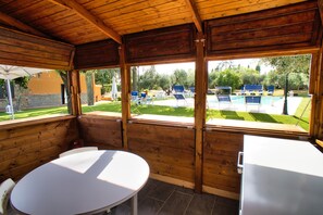 A covered outdoor seating area with a pool view, wooden walls, and a white table. - B&B Casale Ansamagi Relax & Pool (Genzano di Roma)