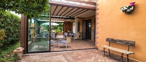 Un patio al aire libre con puerta de vidrio que da a un comedor, un banco y una planta en maceta en la pared.