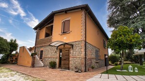 A two-story house with a stone facade, a balcony, and a well-maintained lawn. - B&B Casale Ansamagi Relax & Pool (Genzano di Roma)