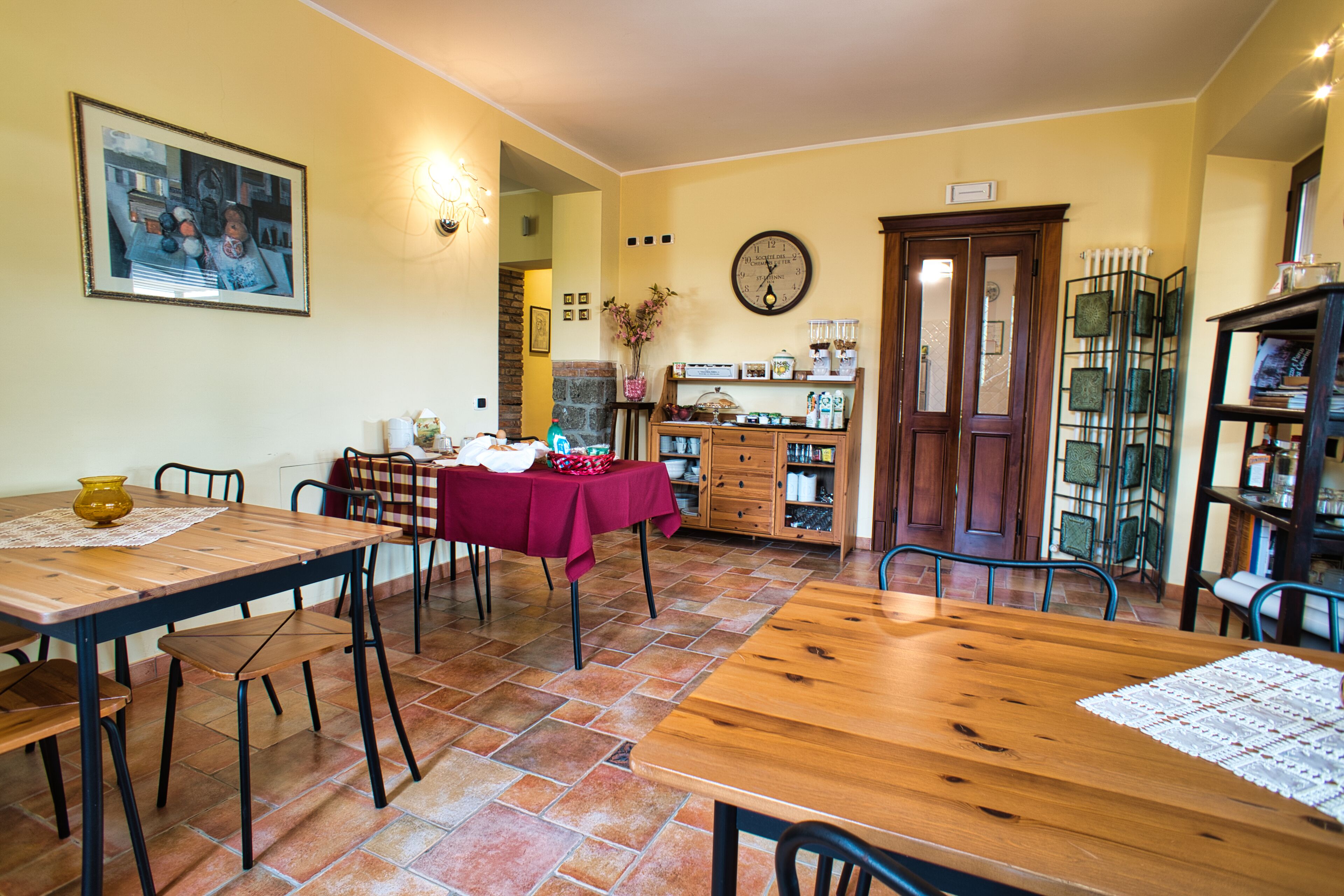 Un comedor con una mesa y sillas de madera, un mantel rojo y un reloj en la pared.