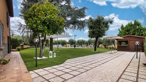 A courtyard with a paved walkway, seating areas, and a small wooden structure. - B&B Casale Ansamagi Relax & Pool (Genzano di Roma)