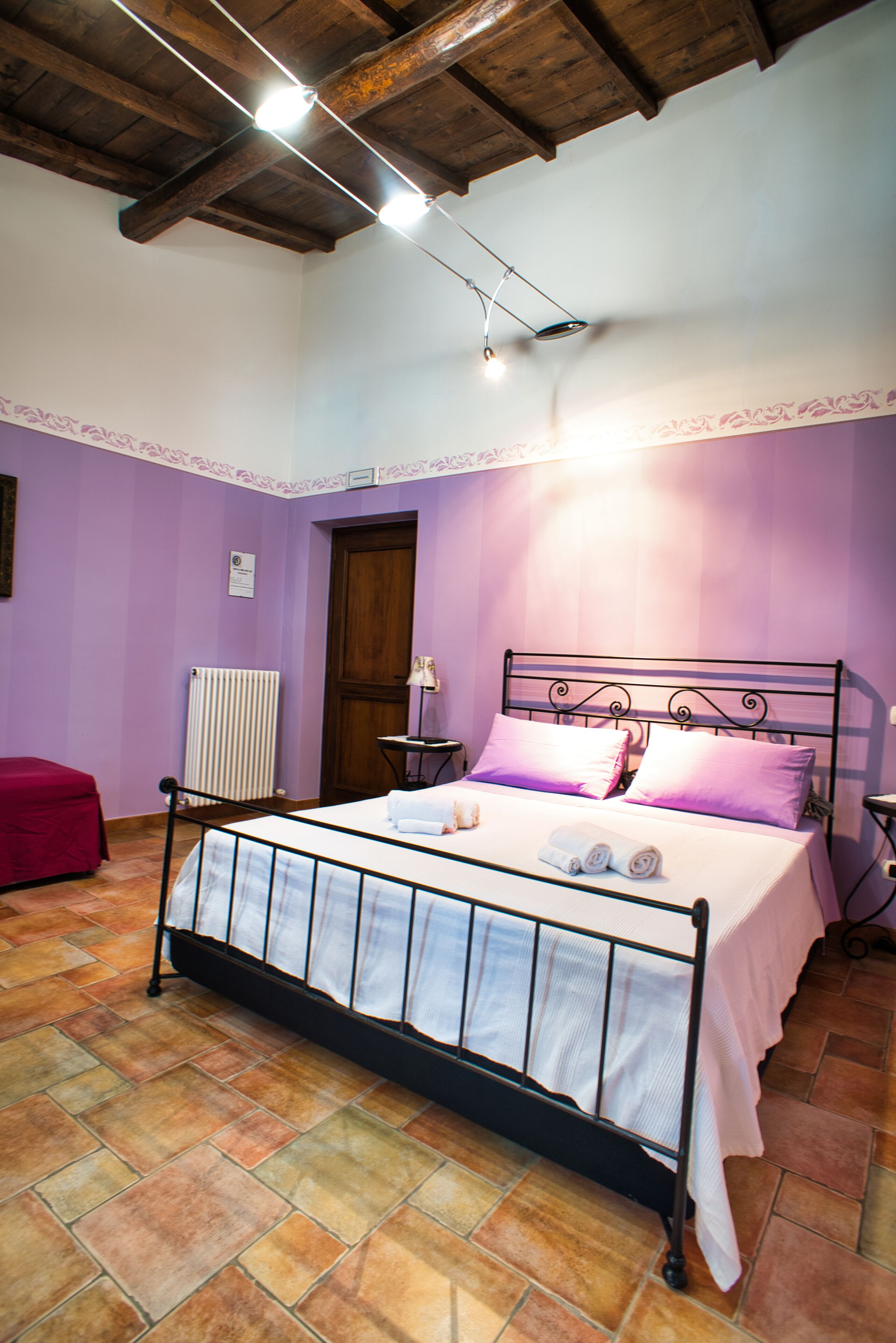 Una camera da letto con un letto, una sedia rossa, un comodino e un termosifone.