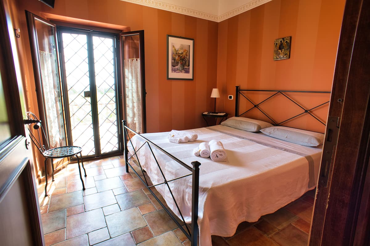 A hotel room with a bed, a chair, a nightstand, and a door leading to a balcony.
