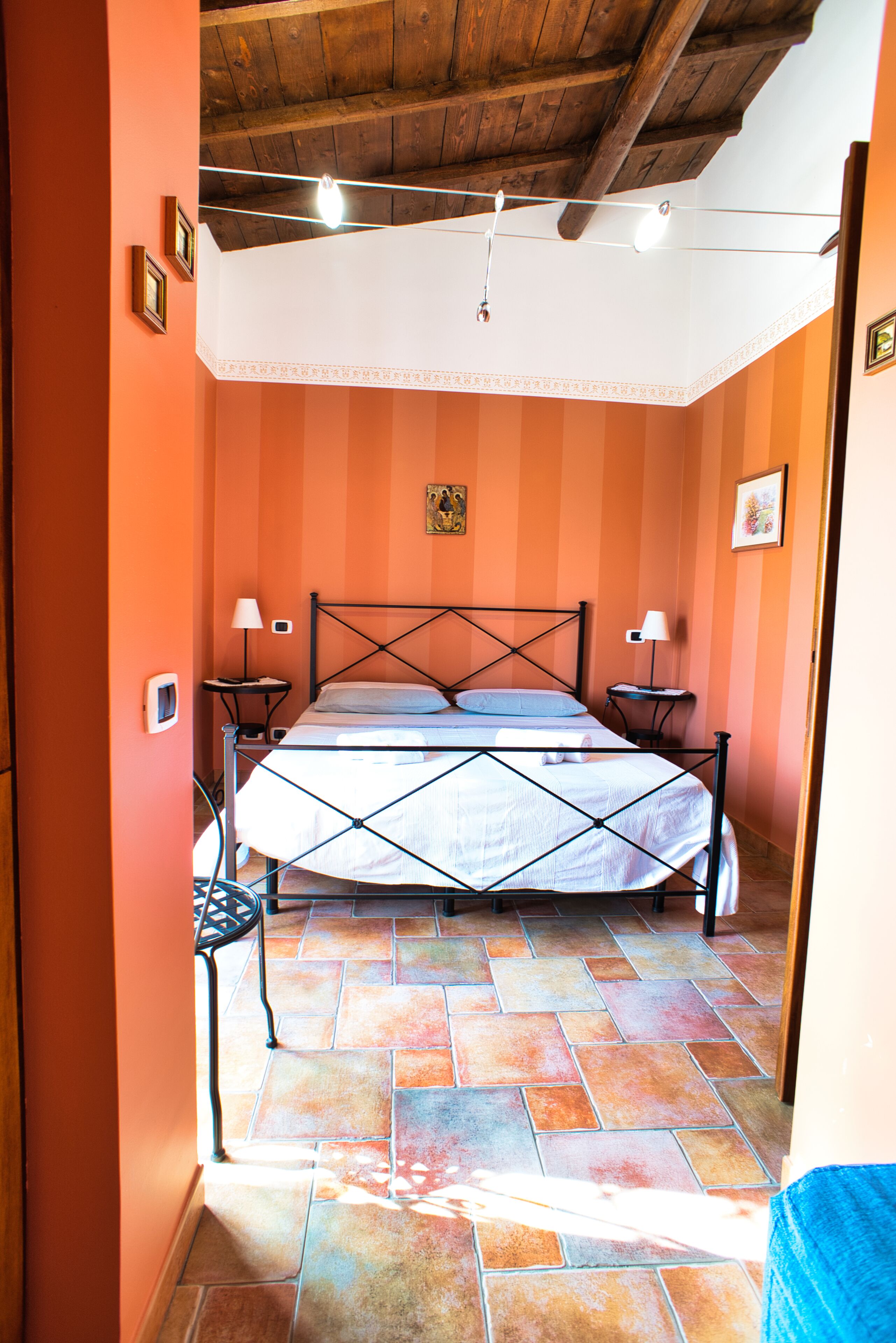 A bedroom with a bed, two bedside tables, a chair, and a wooden ceiling.