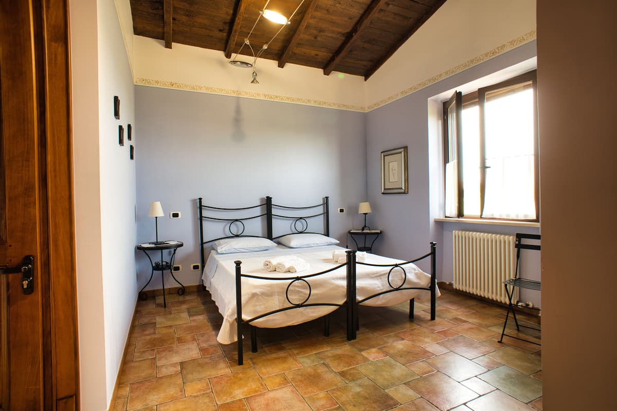A bedroom with a bed, two bedside tables, a radiator, and a window.