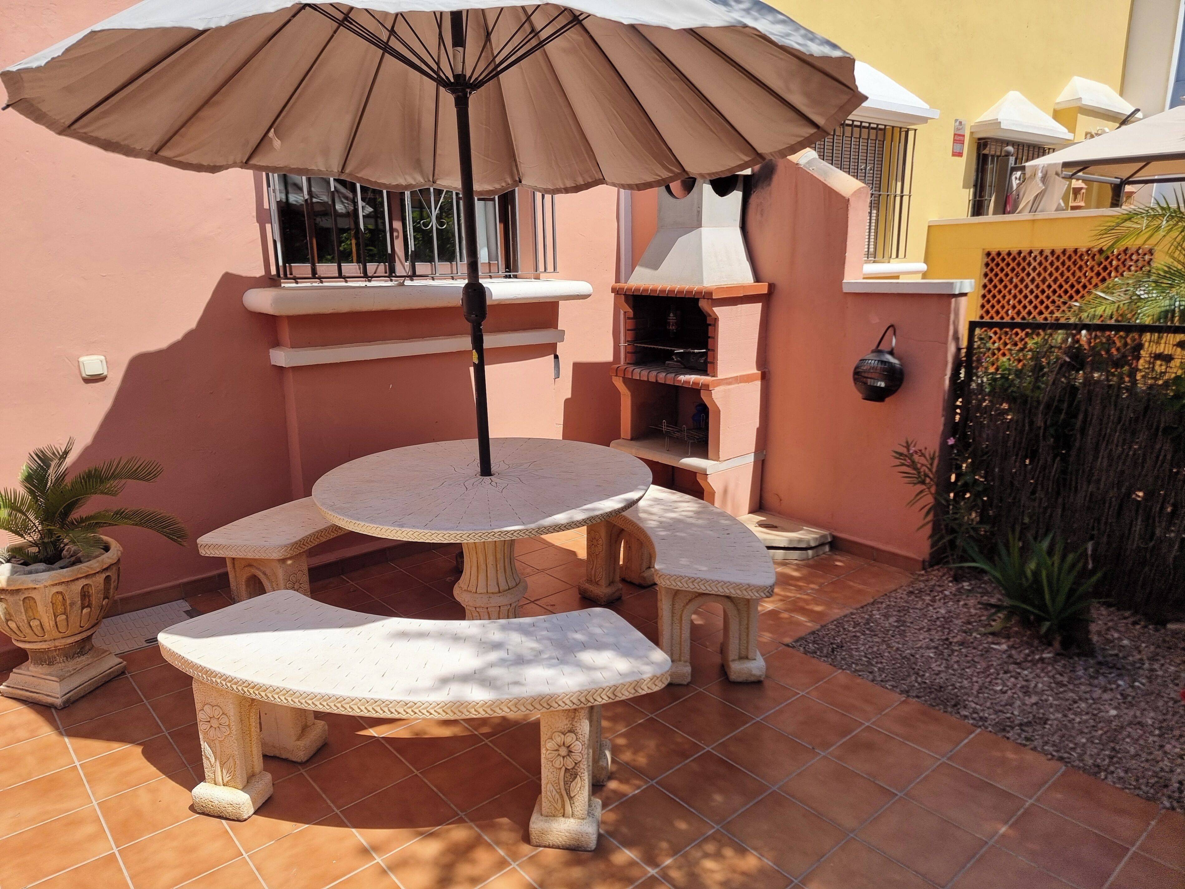 A patio with a round table and benches, an umbrella, and a barbecue grill.