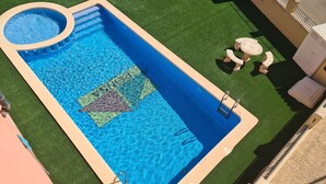 A rectangular swimming pool with a circular hot tub, surrounded by artificial grass, with a small table and chairs nearby. - Three Double Bedroom Townhouse in Lovely Village (San Javier)