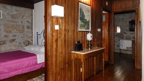 Habitació amb panells de fusta, un llit, una tauleta de nit amb una làmpada i una paret de pedra.