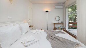 Una habitación de hotel con cama, mesita de noche, lámpara, espejo y vistas al exterior.