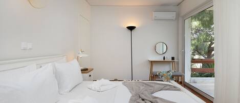 A hotel room with a bed, a bedside table, a lamp, a mirror, and a view of the outdoors.
