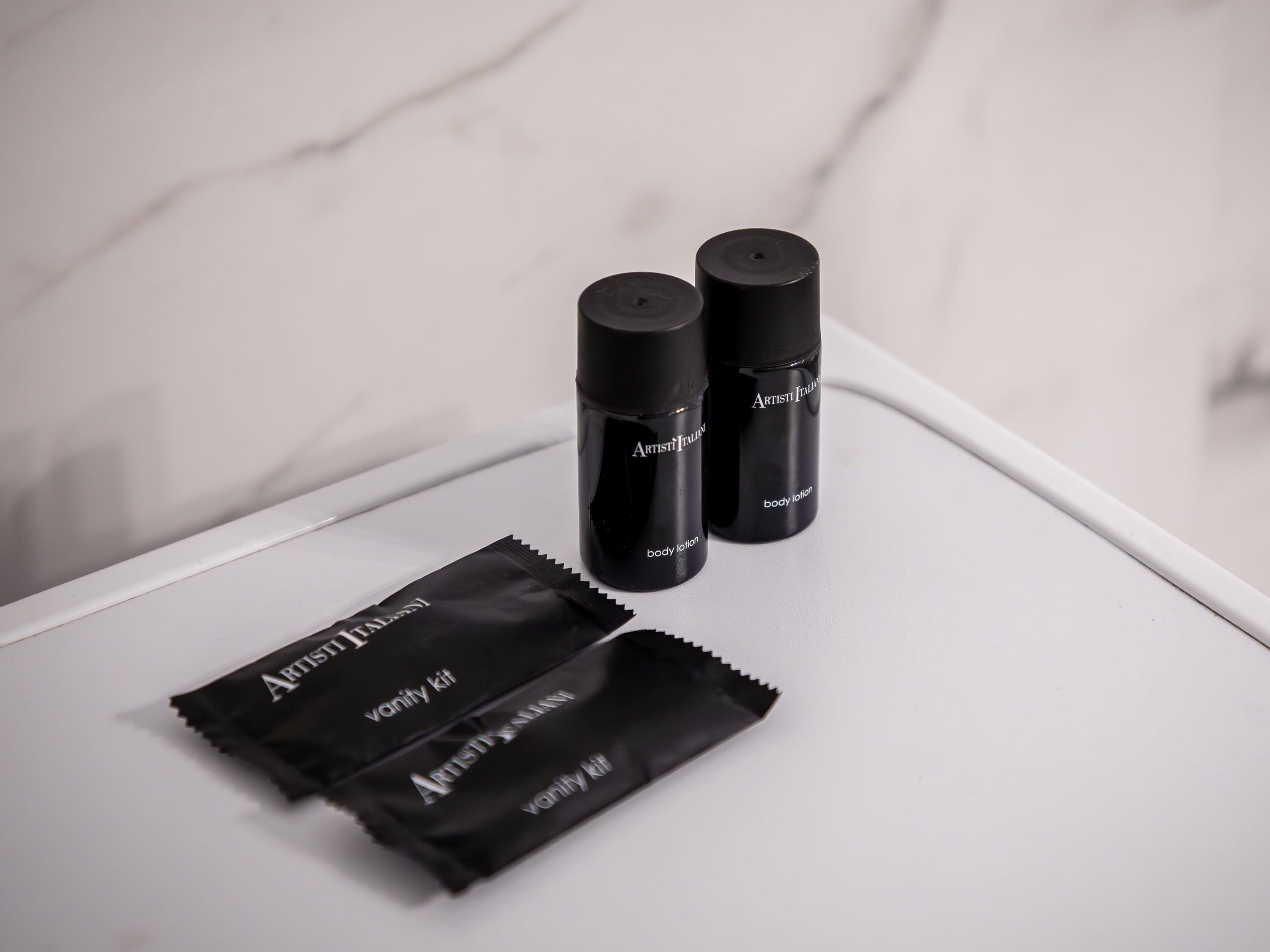 Two black bottles labeled 'Artist Italia body lotion' and a black packet labeled 'Artist Italia vanity kit' on a white surface.