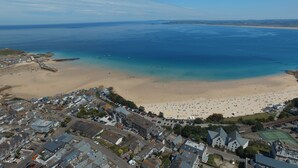 An aerial view of a coastal town with a beach, houses, and a tennis court. - The Golden Hind (St Ives)