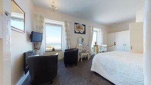 A hotel room with a bed, a desk with a chair, a vanity with a mirror, and a television. - The Golden Hind (St Ives)