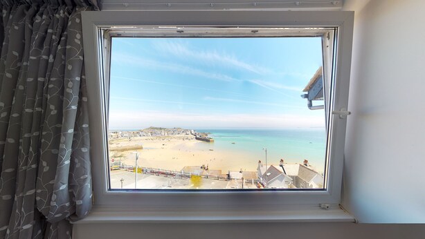 A window with a view of a beach, a promenade, and buildings in the distance. - The Golden Hind (St Ives)