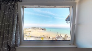 A window with a view of a beach, a promenade, and buildings in the distance. - The Golden Hind (St Ives)
