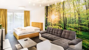 Una habitación de hotel moderna con una cama grande, un sofá gris y un mural temático de bosque.