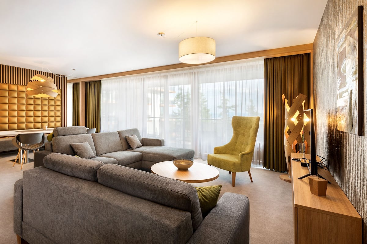 A modern living room with a sectional sofa, a round coffee table, a high-back armchair, and a dining area with a white table and chairs.