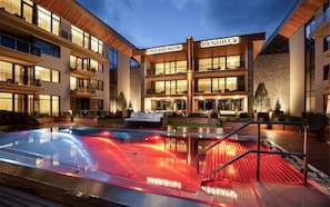 Un resort moderno con zona de piscina, varios balcones e iluminación destacada en la entrada.