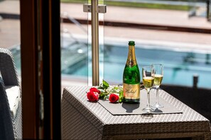Una mesa de mimbre con una botella de champán y dos copas, acompañada de rosas rojas, cerca de una piscina.