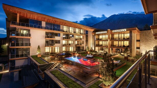 Un hotel de varios pisos con piscina, mobiliario exterior y vistas a la montaña.