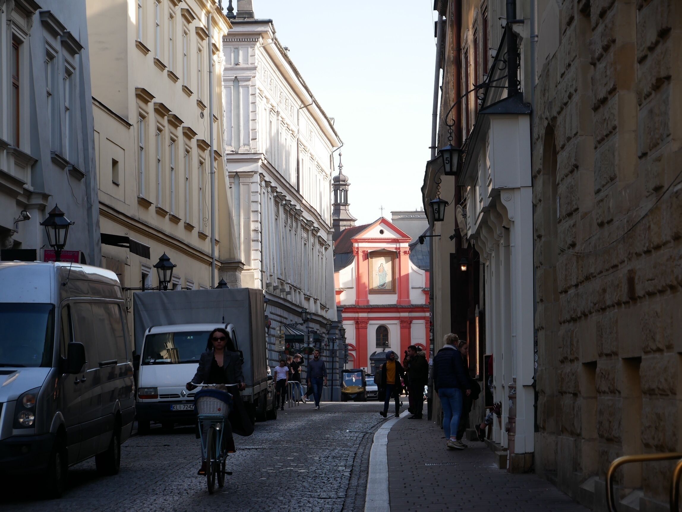 A cobblestone street with buildings on either side, a cyclist, and pedestrians.