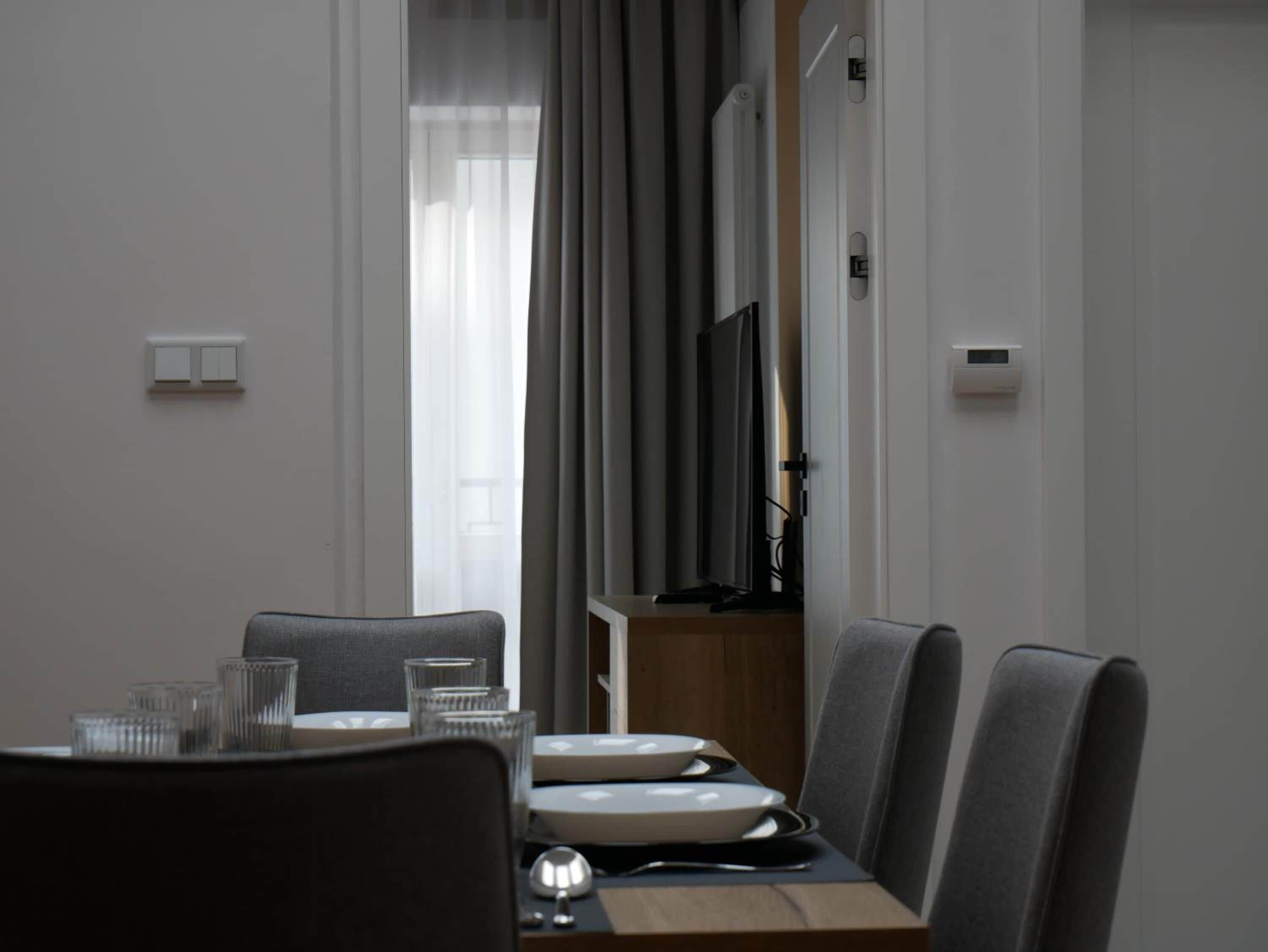 Un comedor moderno con una mesa de madera, sillas tapizadas de gris y un televisor montado en la pared.